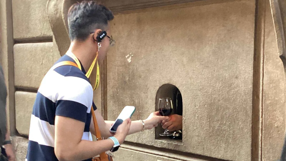 A glass handed through a historic buchetta del vino wine window on a wine tasting walk in Florence